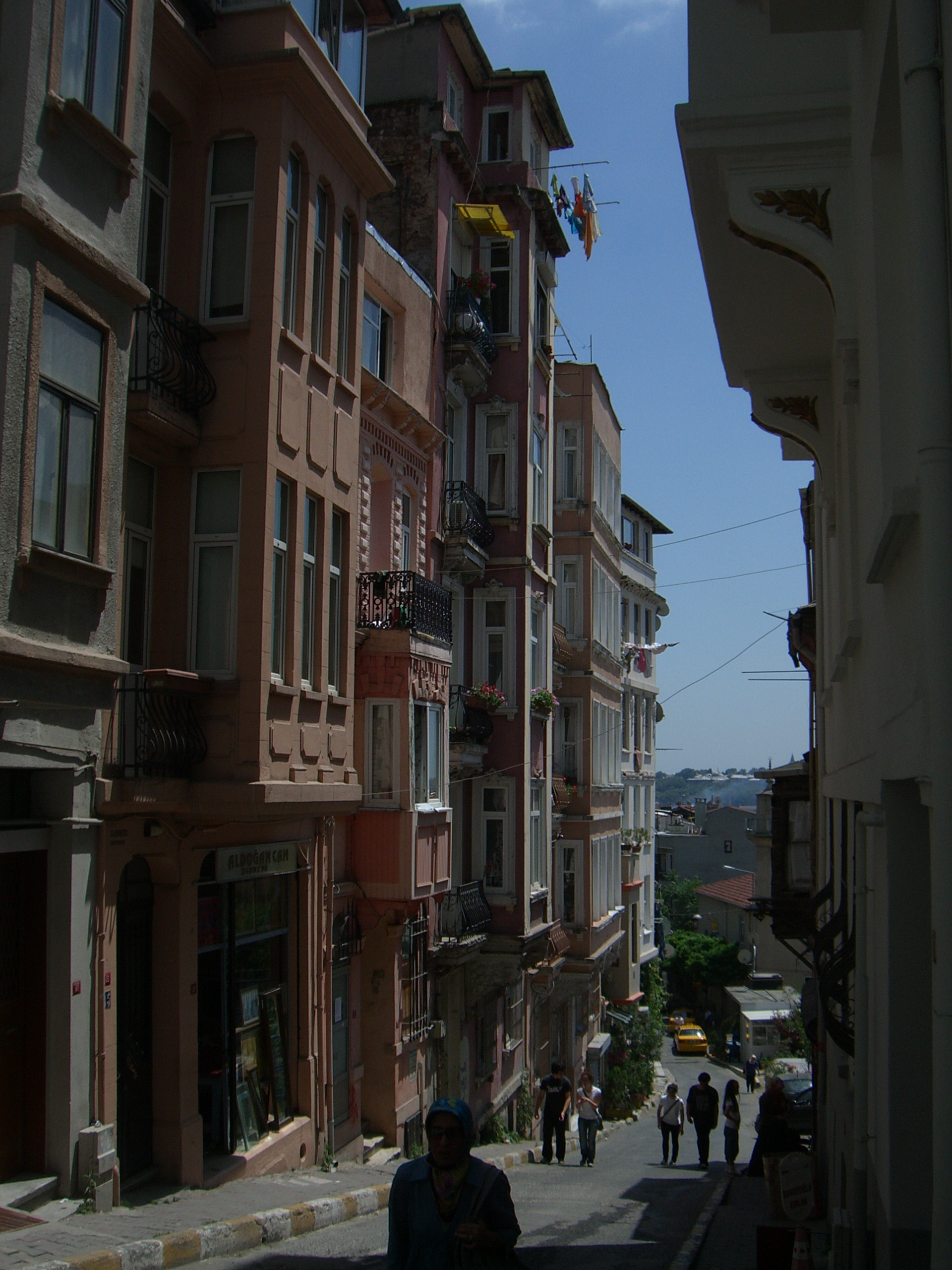 A steep narrow Cihangir street of tall pastel apartment buildings with iron balconies, dropping away downhill