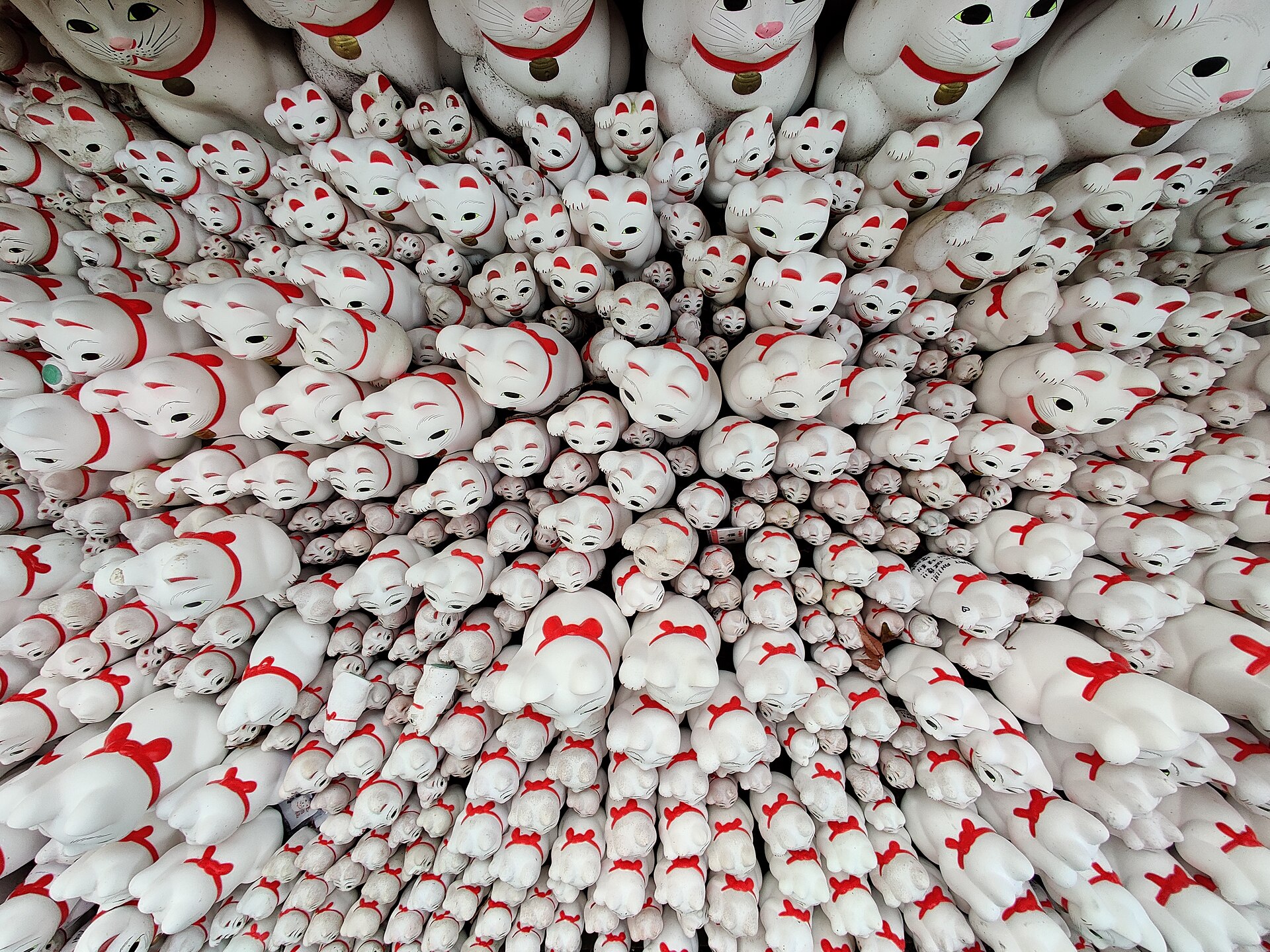 Hundreds of white maneki-neko lucky cat figurines with red collars packed onto the shelves at Gotokuji Temple