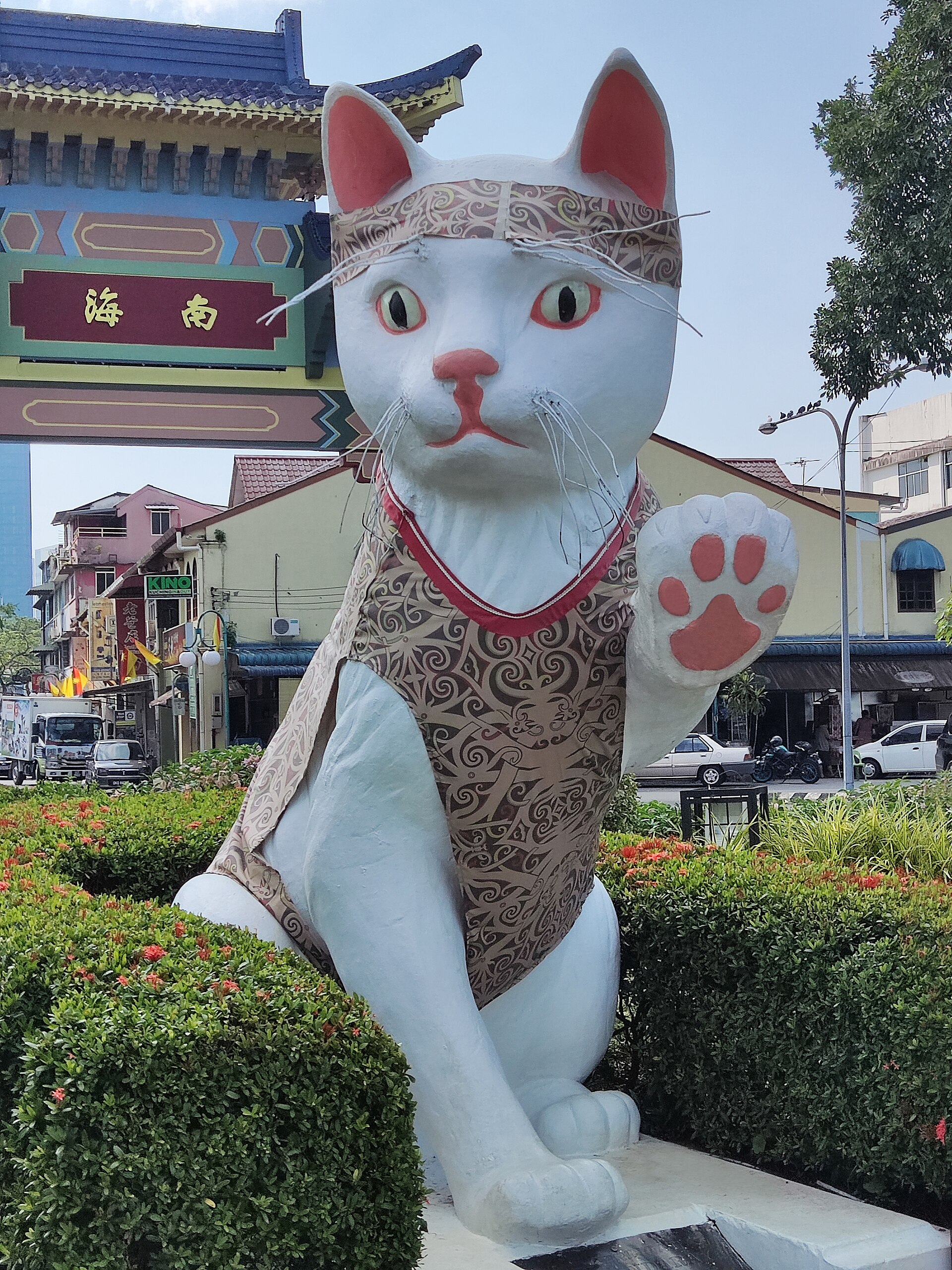 The Great Cat of Kuching, a giant white cat statue with a raised paw, dressed in a patterned vest and headband, at the Padungan end of town