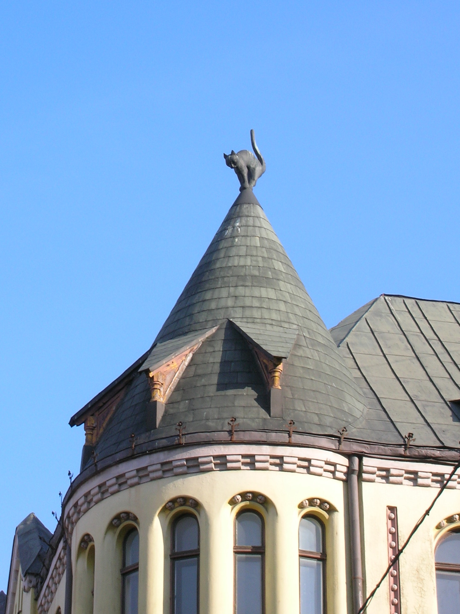 The cat on the turret of the Cat House, back arched, tail up