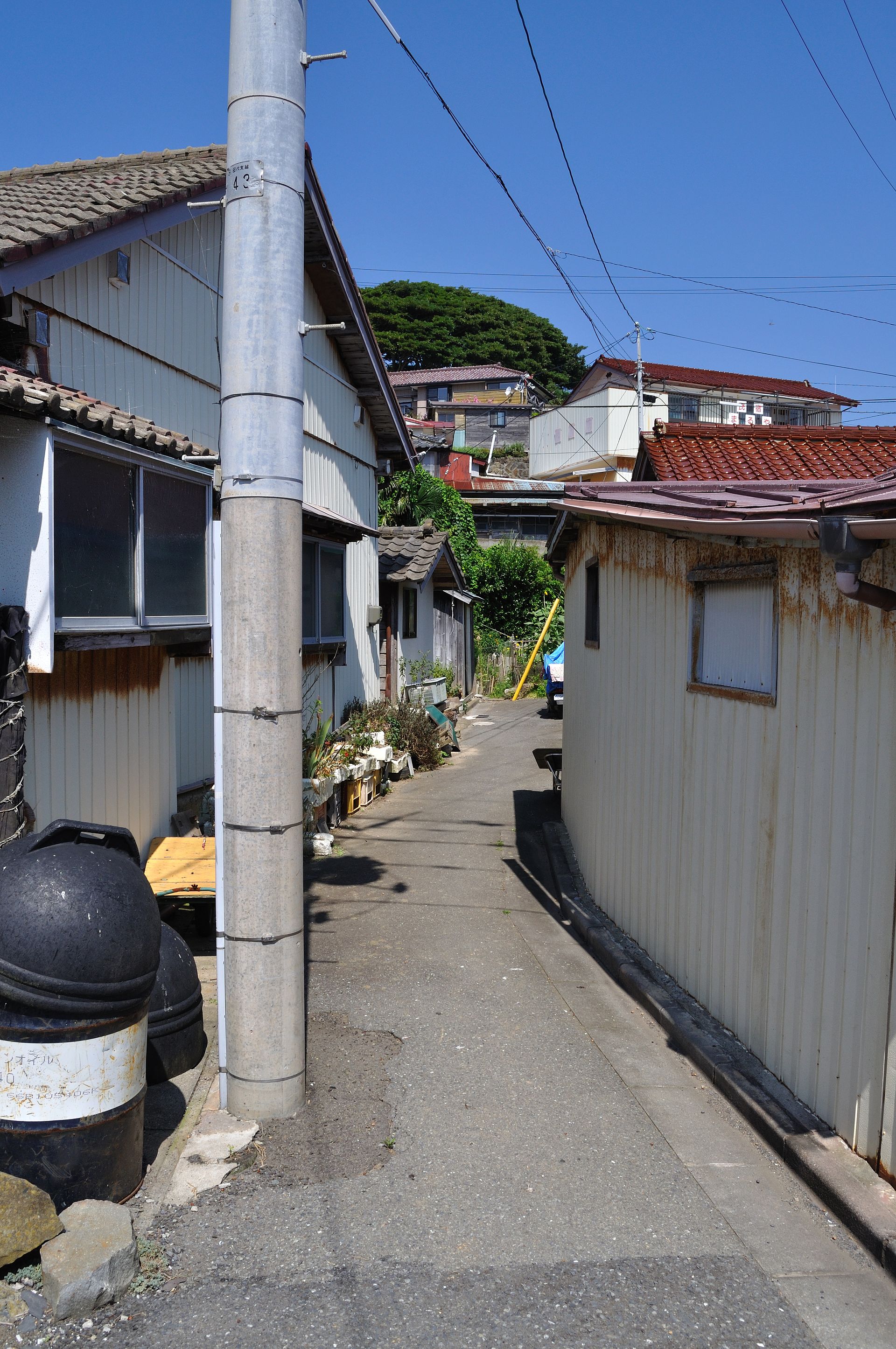 A narrow lane between corrugated-iron houses on Tashirojima, oil drums by the wall
