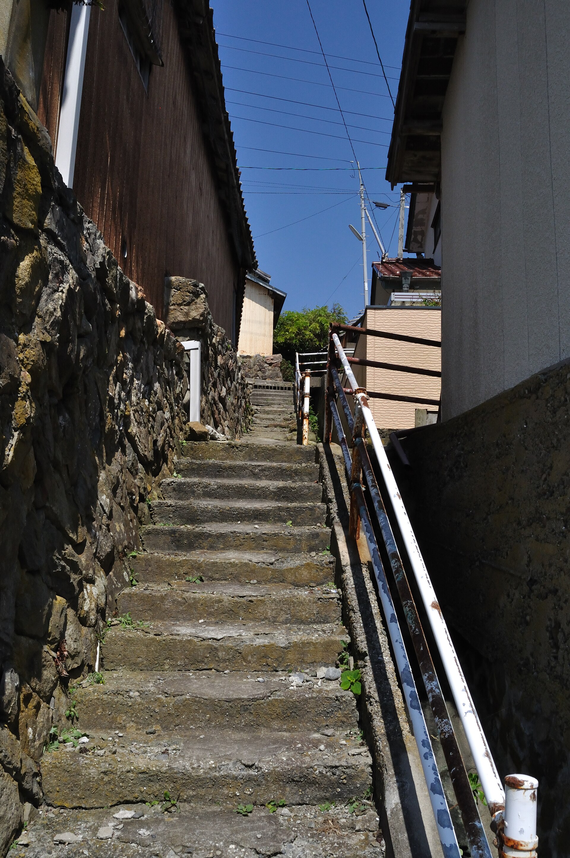 A steep flight of worn stone steps between a stone wall and a wooden house on Tashirojima