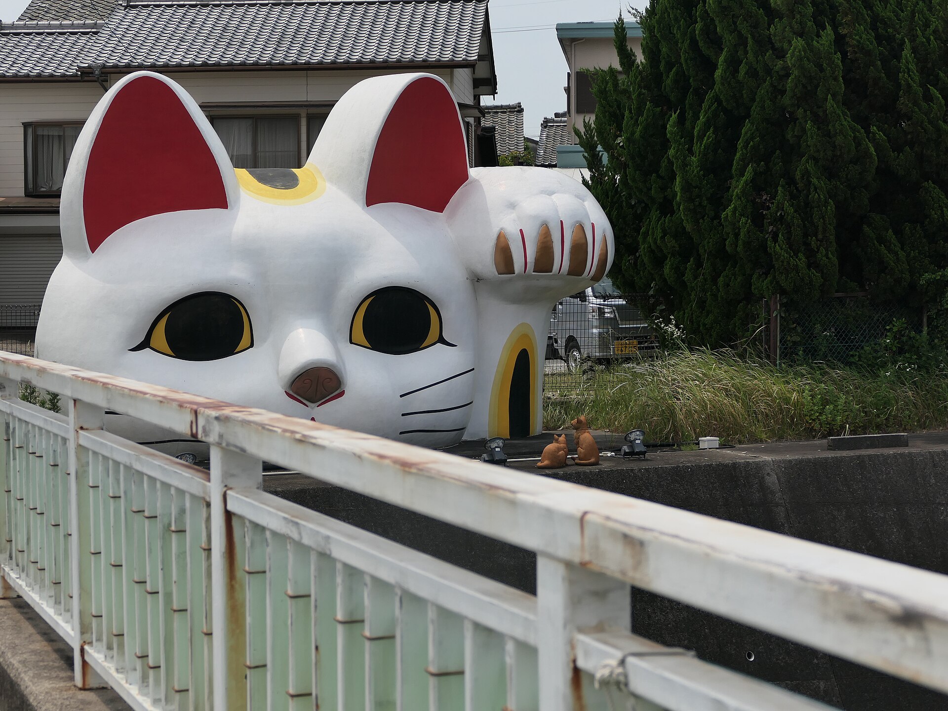 Tokonyan, the giant ceramic lucky cat head with a raised paw, peering over a wall in Tokoname