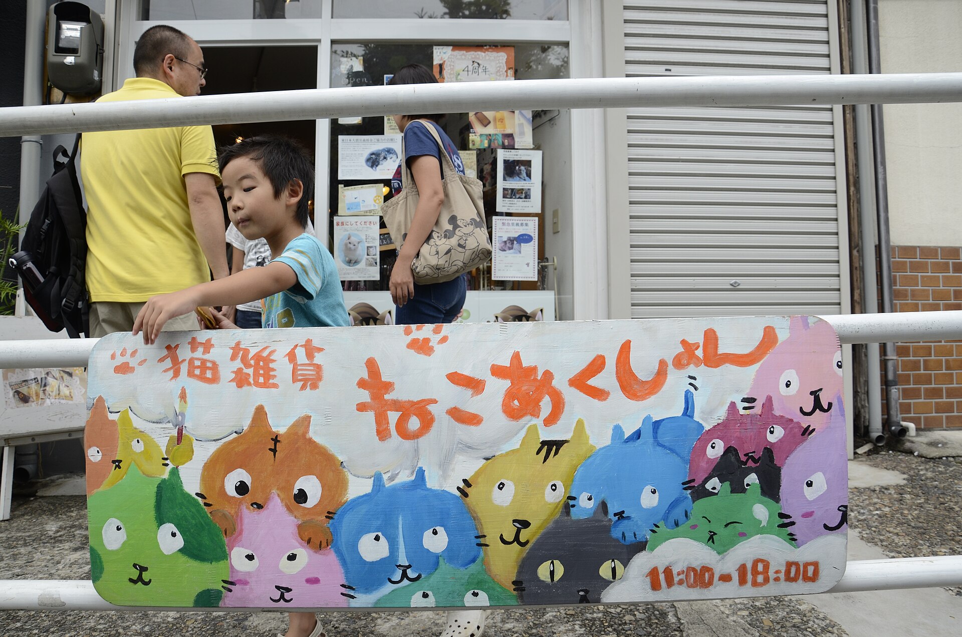 A family outside the Neco Action cat goods shop in Yanaka, Tokyo, behind a painted sign of cartoon cats